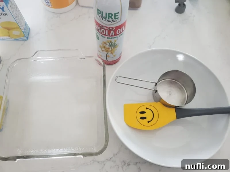 Basic kitchen equipment for baking a casserole: a glass baking dish, a spatula, a measuring cup, and a large mixing bowl, all arranged on a clean white countertop.