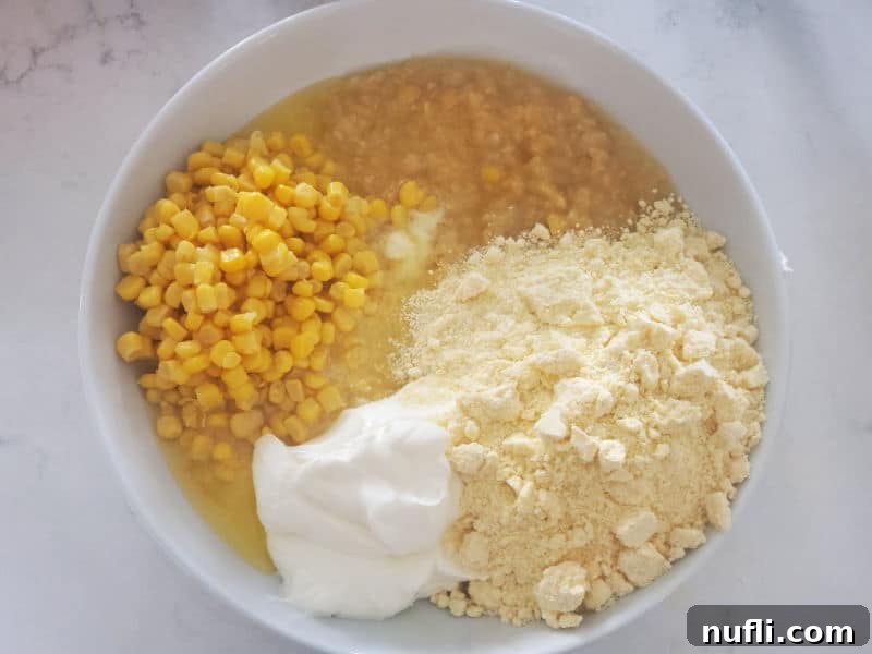 All ingredients for Creamed Corn Casserole are placed unmixed in a large white bowl, ready for combining.