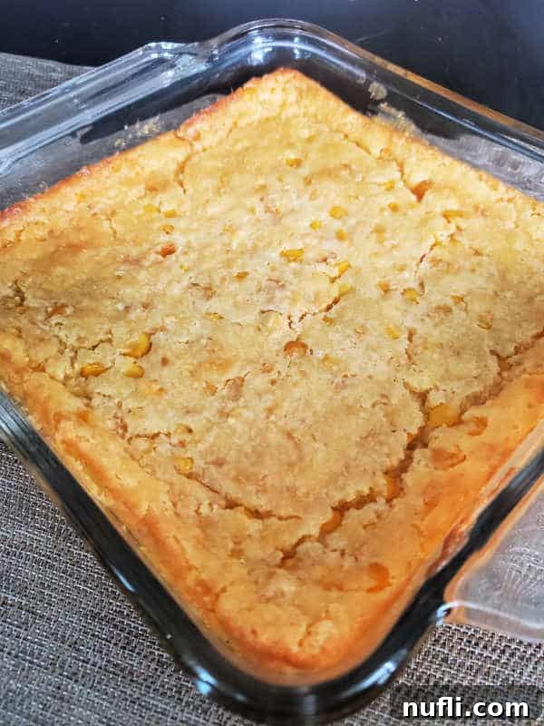 Creamed corn casserole baking in a glass dish, showing a lightly browned top.
