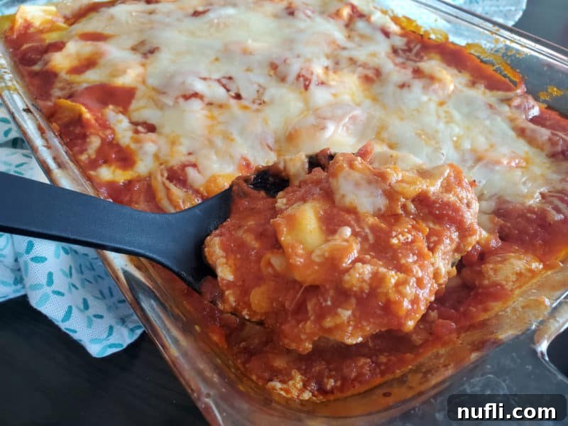 A black spoon scooping a generous portion of hot, cheesy lazy lasagna from a glass casserole dish.