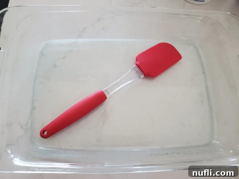 A red spatula resting in a glass casserole dish, ready for assembling the lazy lasagna.