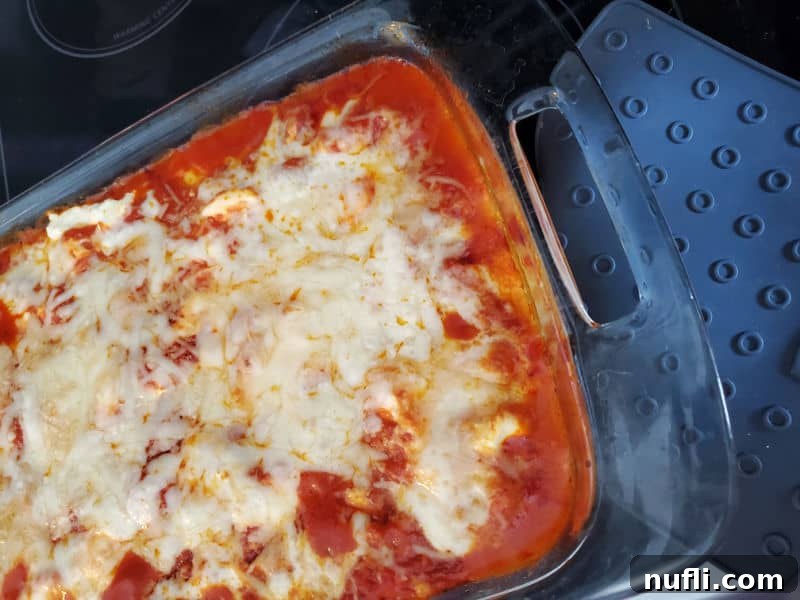 A baked lazy lasagna in a glass casserole dish, freshly removed from the oven, with a silicone oven mitt beside it.