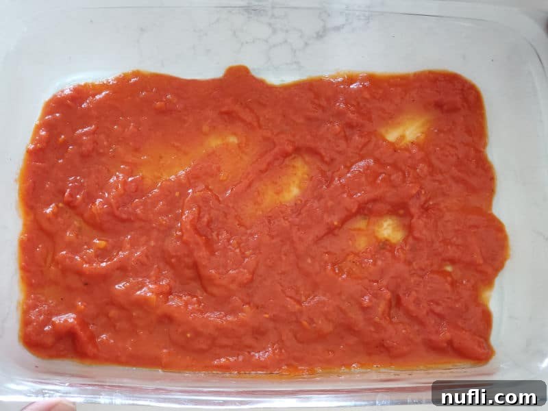 A generous layer of marinara sauce spread evenly across the bottom of a clear glass casserole dish.