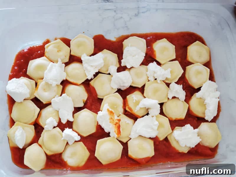 A layer of creamy ricotta cheese spread over the ravioli and marinara sauce in a glass casserole dish, for added richness.