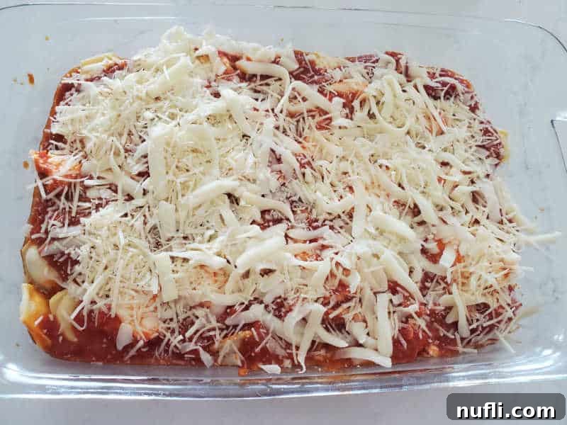 The final layer of shredded mozzarella cheese generously sprinkled over the marinara and ravioli, ready for baking.