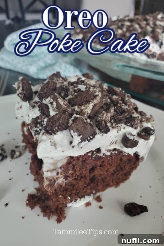 A square slice of Oreo Poke Cake on a white plate, showcasing its layers of chocolate cake, pudding, and whipped topping with crushed Oreos. The full cake in the baking dish is blurred in the background.