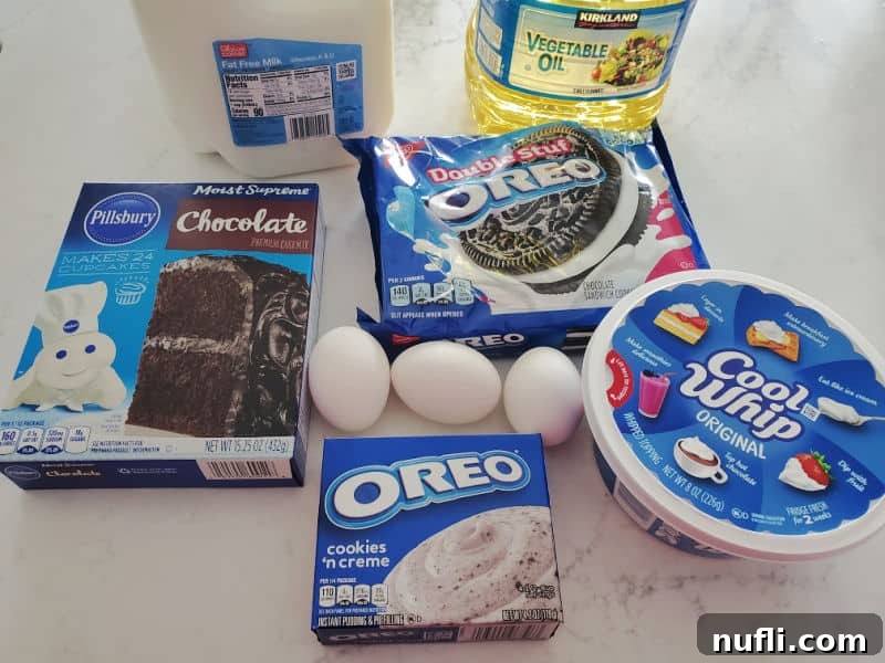 Ingredients for Oreo Poke Cake including milk, vegetable oil, chocolate cake mix, Double Stuff Oreos, eggs, Oreo pudding mix, and cool whip, arranged on a white counter.