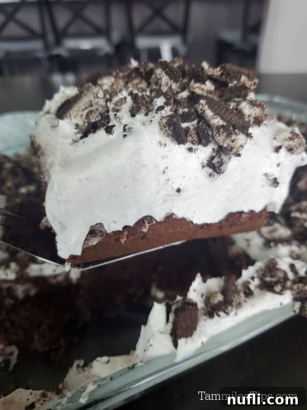Spatula lifting a square slice of Oreo Poke Cake above the baking dish, ready to be served.