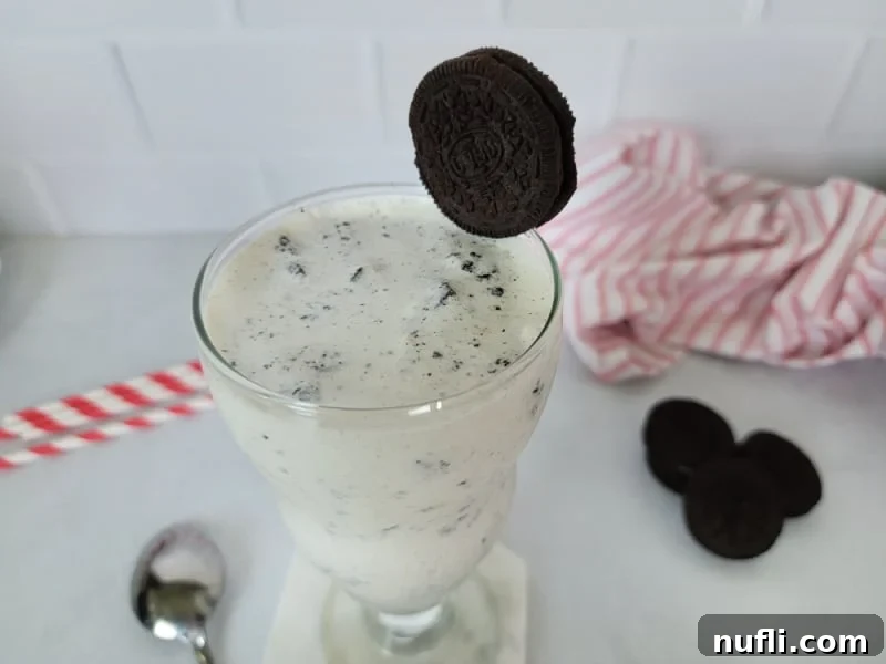 Whip Up a Perfect Oreo Milkshake 4 Oreo Shake in a glass mug with a spoon, garnished with a whole Oreo and surrounded by loose Oreos.