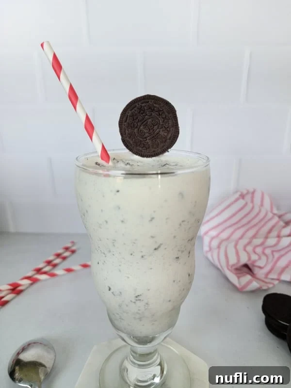 Whip Up a Perfect Oreo Milkshake 5 Oreo Milkshake in a tall glass with a red striped straw and Oreo garnish on a dark background.
