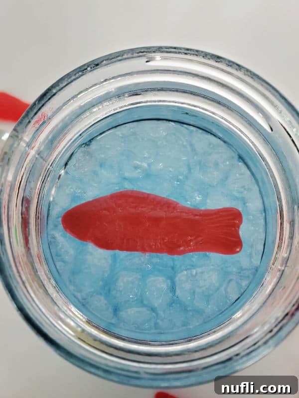 Homemade Sonic Ocean Water Drink Guide 3 A mason jar filled with blue Sonic Ocean Water, topped with ice cubes and a playful Swedish Fish candy, ready to be enjoyed.