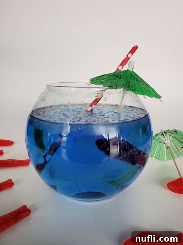 A vibrant blue Sonic Ocean Water drink served in a fishbowl glass, complete with a green tropical umbrella, a red striped straw, and floating Swedish Fish candies.