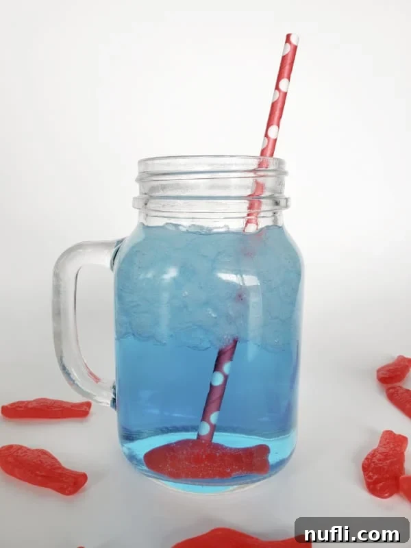 A close-up of a blue Sonic Ocean Water drink in a Mason jar, garnished with a red polka dot straw and Swedish Fish candy.