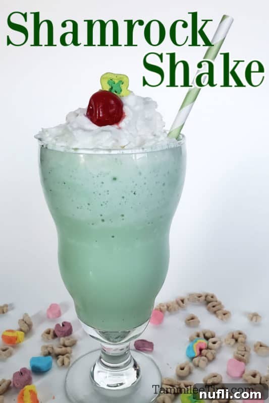 A perfectly blended Shamrock Shake in a clear glass, topped with a generous swirl of whipped cream and a bright red maraschino cherry.