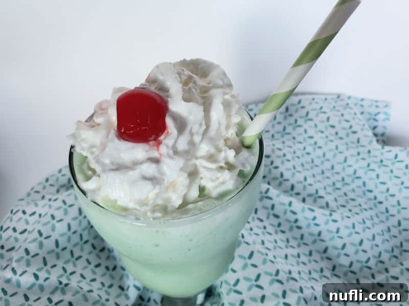 A top-down view of a Shamrock Shake, showcasing the vibrant green color, fluffy whipped cream, and a single maraschino cherry on top.