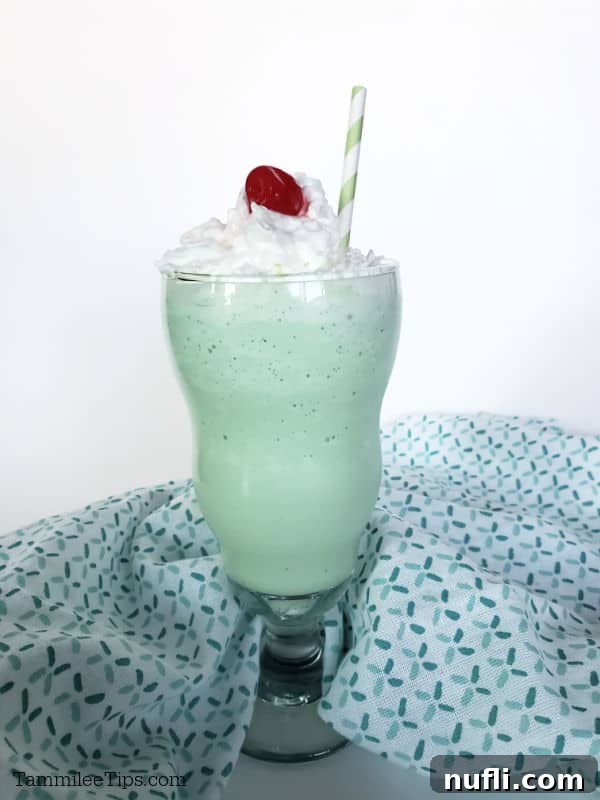 A close-up of a Shamrock Shake in a tall glass, with a single green paper straw, placed beside a neatly folded cloth napkin.