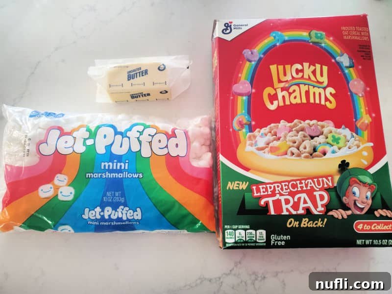 Ingredients for Lucky Charms treats: butter, mini marshmallows, and Lucky Charms cereal laid out on a white counter.