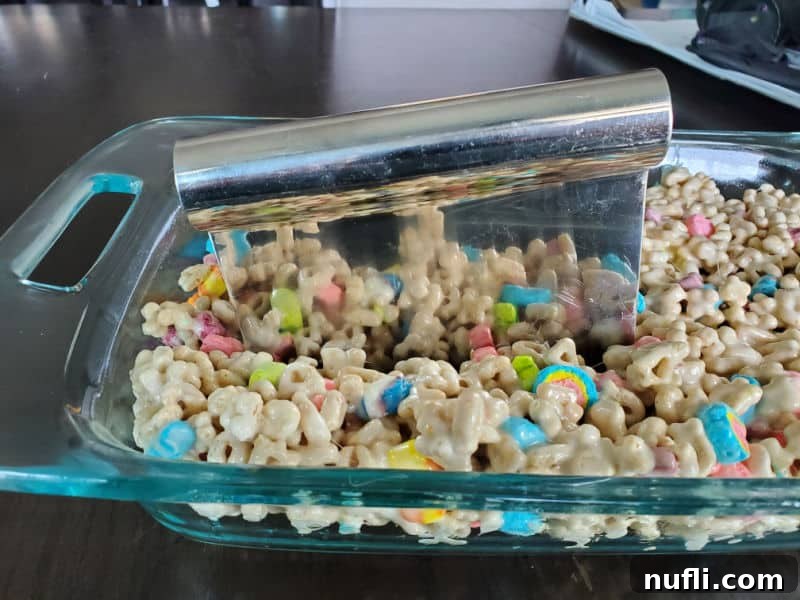 A pastry dough cutter slicing through a pan of homemade Lucky Charms treats in a glass baking dish.