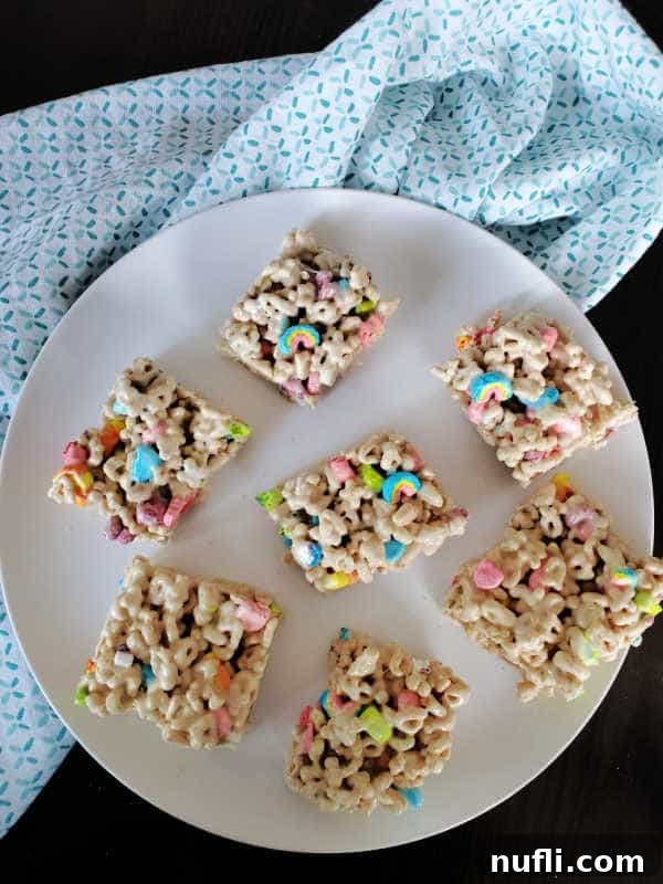 Squares of Lucky Charms treats arranged on a white circular plate next to a folded cloth napkin, ready for serving.