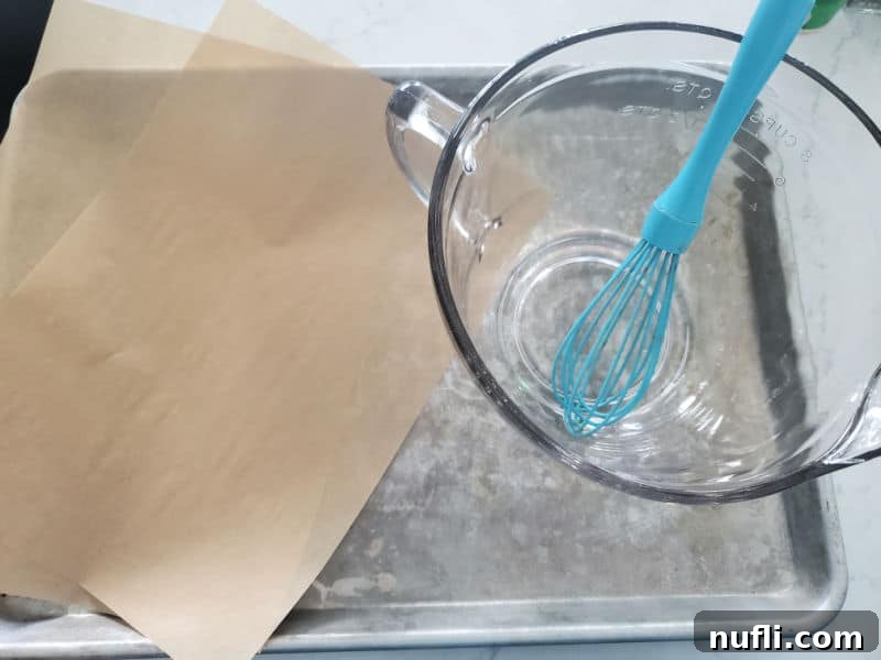 Baking sheet with parchment paper, a glass bowl for mixing, and a whisk, ready for preparing dill oyster crackers.