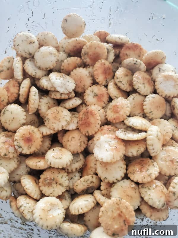 Close-up of a glass bowl brimming with golden-brown, seasoned dill oyster crackers, showcasing their crunchy texture.