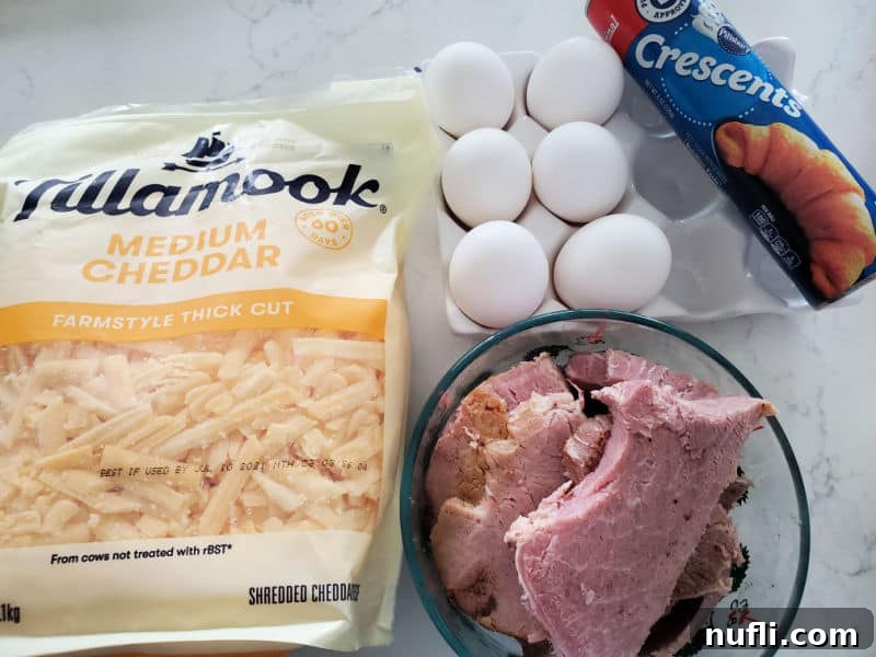 Shredded cheddar cheese, eggs, crescent roll, and ham in a bowl sitting on a white counter. 