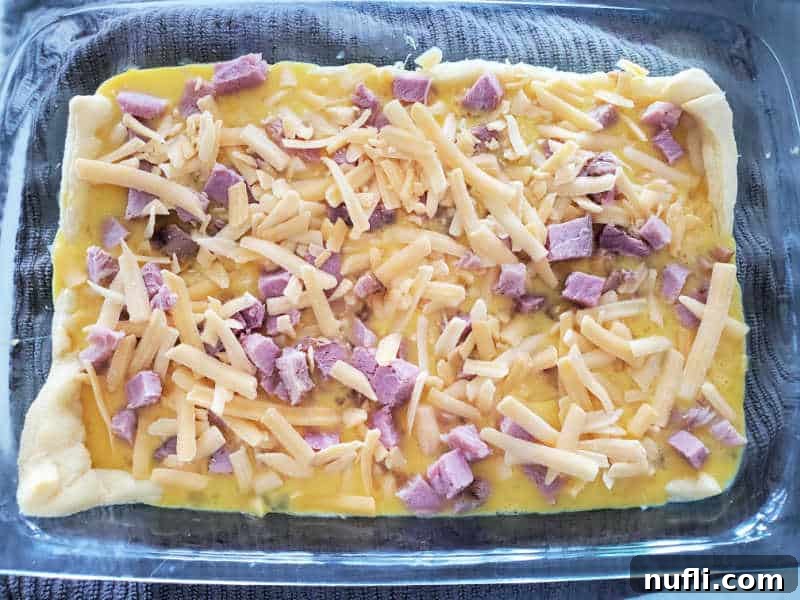 crescent roll topped with egg, ham and shredded cheese in a glass baking dish. 