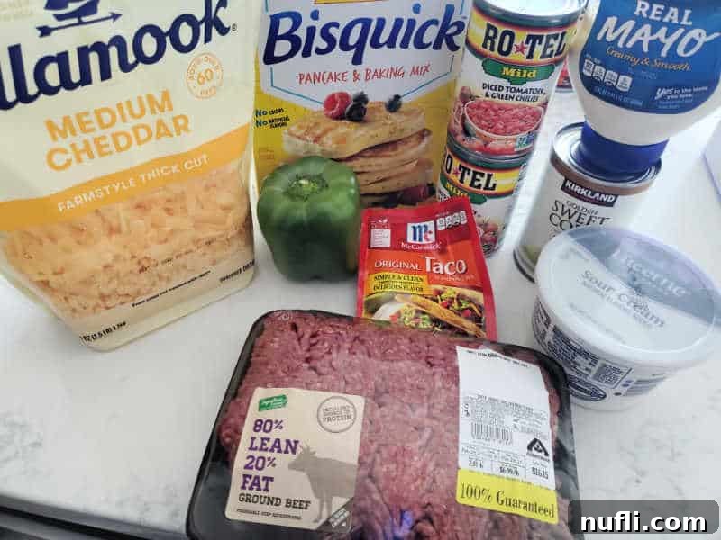 cheddar cheese, bisquick, rotel cans, mayo, corn, taco seasoning, green bell pepper, sour cream, and ground beef on a white counter 