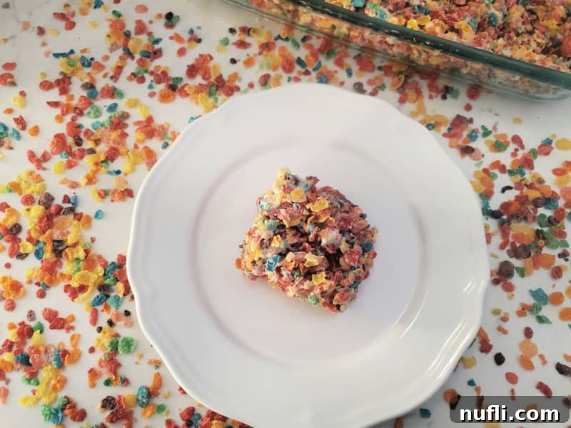 Vibrant Fruity Pebbles Rice Krispie Treats 6 Square fruity pebbles rice crispy treat in the center of a white plate surrounded by cereal and the baking dish