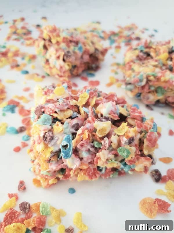 Vibrant Fruity Pebbles Rice Krispie Treats 7 Squares of Fruity Pebbles rice crispy teats on a white counter with additional fruity pebbles cereal