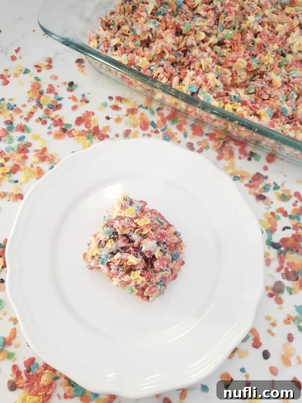 Vibrant Fruity Pebbles Rice Krispie Treats 8 Fruity Pebbles Rice Crispy Treat on a white plate next to a glass baking dish with fruity pebbles treats.