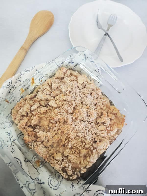 Easy Bisquick Apple Cobbler 4 Bisquick apple cobbler in a baking dish next to a wooden spoon, white plate with forks.