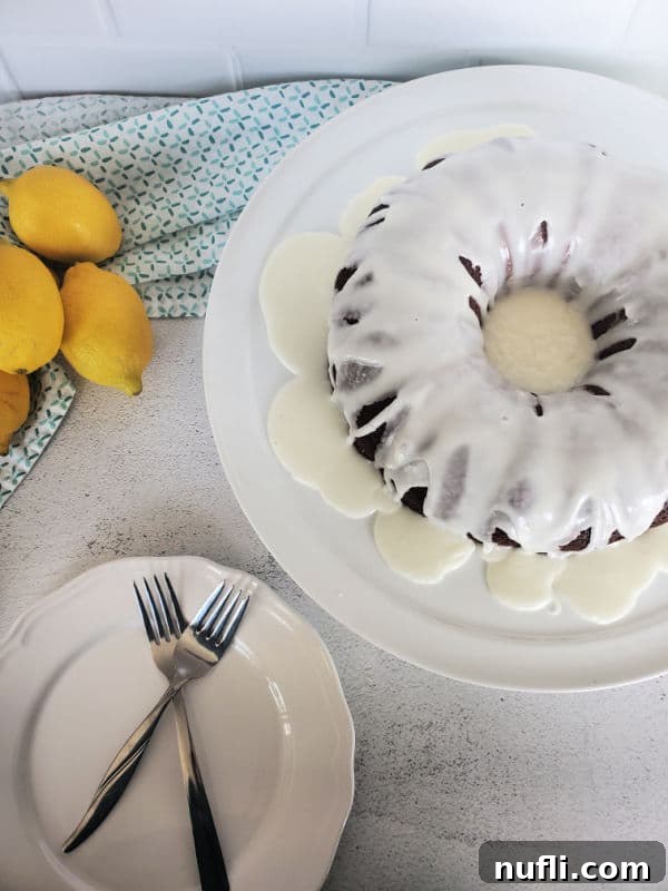 A complete Mountain Dew Bundt Cake on a white platter, elegantly presented alongside a bowl of fresh lemons and a plate with forks, indicating it's ready for a gathering.