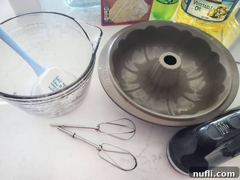 Essential baking equipment laid out: a glass mixing bowl, a bundt cake pan, various whisks, and a hand mixer, all neatly arranged and ready for the baking process.