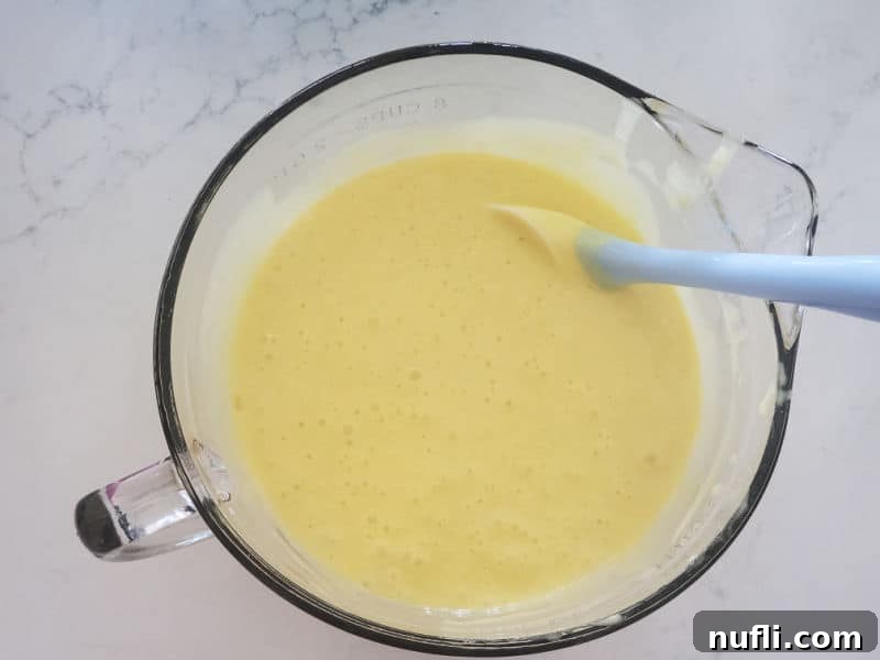 Smooth, well-mixed cake batter in a clear glass bowl, with a spatula dipped in, indicating readiness for baking.