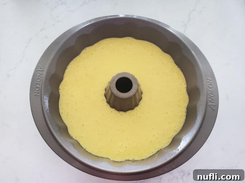 Unbaked cake batter neatly poured into a greased bundt cake pan, perfectly prepared for oven baking.