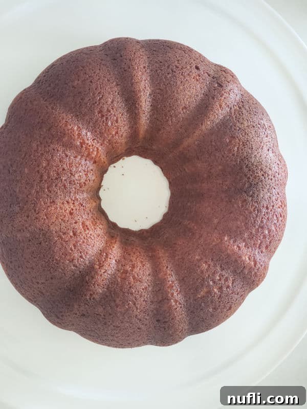 A freshly baked, golden-brown bundt cake cooling on a pristine white platter, showcasing its intricate fluted design.