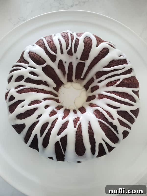 A beautifully glazed bundt cake with luscious white icing cascading down its sides, resting on a pristine white platter, ready for presentation.