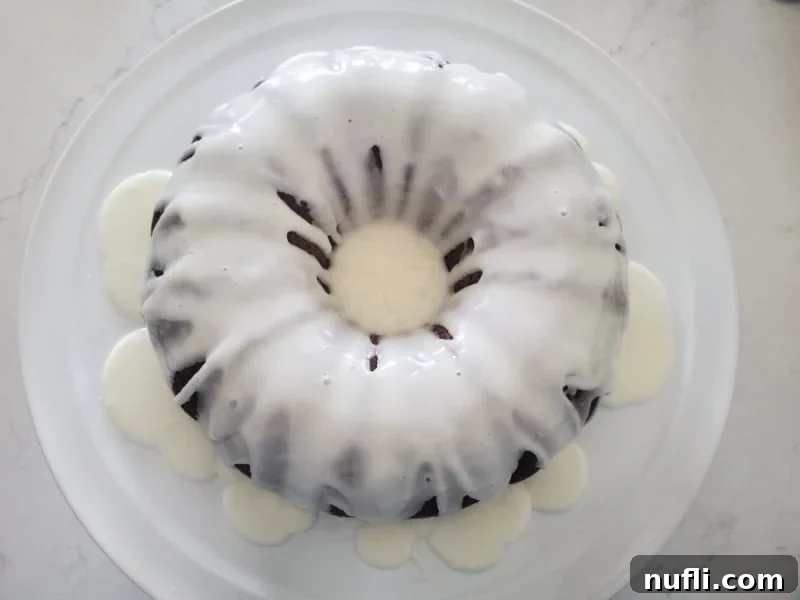A delectable bundt cake generously covered in a shimmering icing glaze, presented on a clean white platter, highlighting its inviting texture and sweetness.