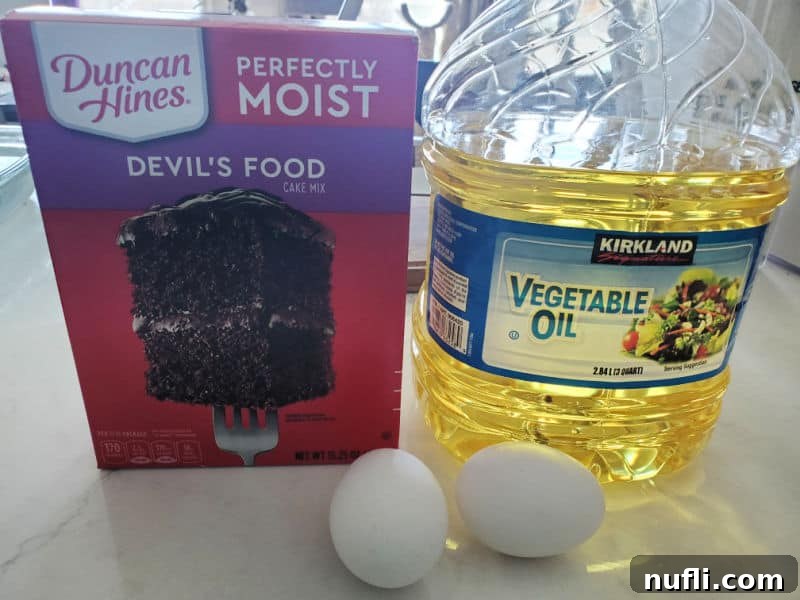Ingredients for chocolate cake mix cookies: a box of Devil's Food cake mix, vegetable oil, and two eggs laid out on a kitchen counter.