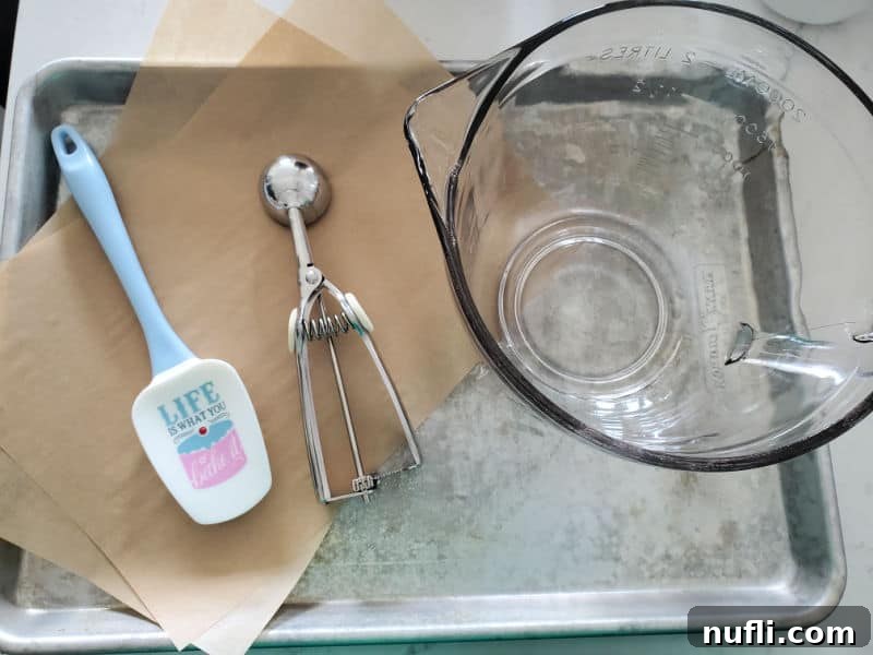 A baking sheet with a mixing bowl, cookie scoop, and spatula, ready for making cookies.