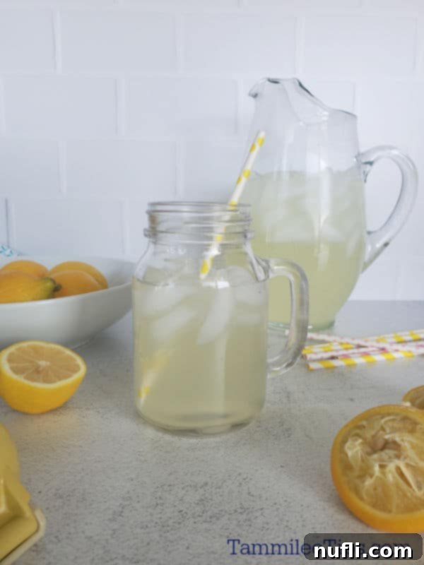 Chick Fil A Lemonade in a mason jar glass with a paper straw next to a pitcher of lemonade and bowl of lemons. 