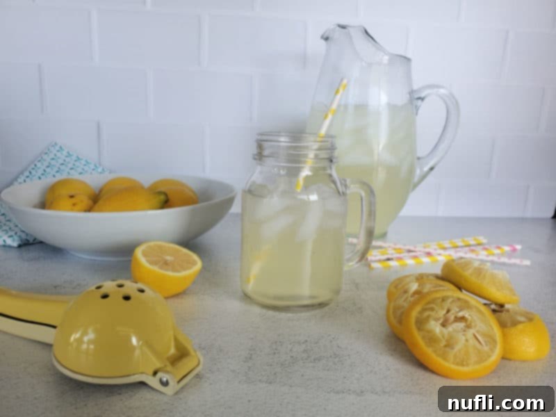 lemonade in a pitcher and a mason jar glass near a bowl of lemons, lemon juicer, and squeezed lemons
