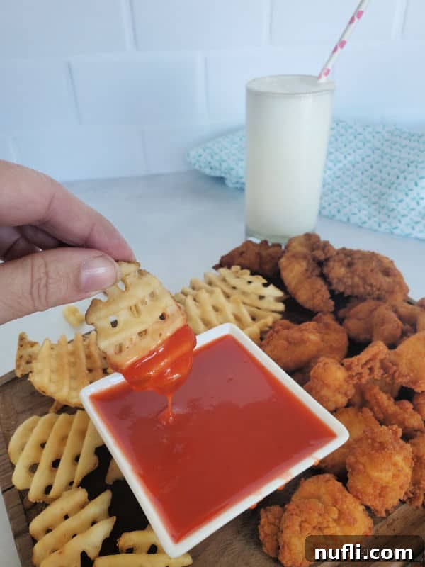 French fry dipping into Polynesian Sauce Chick Fil A copy cat with additional French fries and chicken surrounding the bowl.