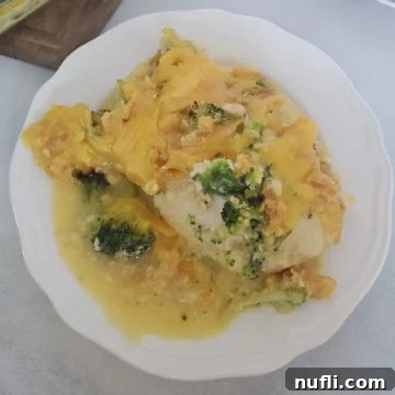 broccoli cheddar chicken on a white plate next to a wooden cutting board