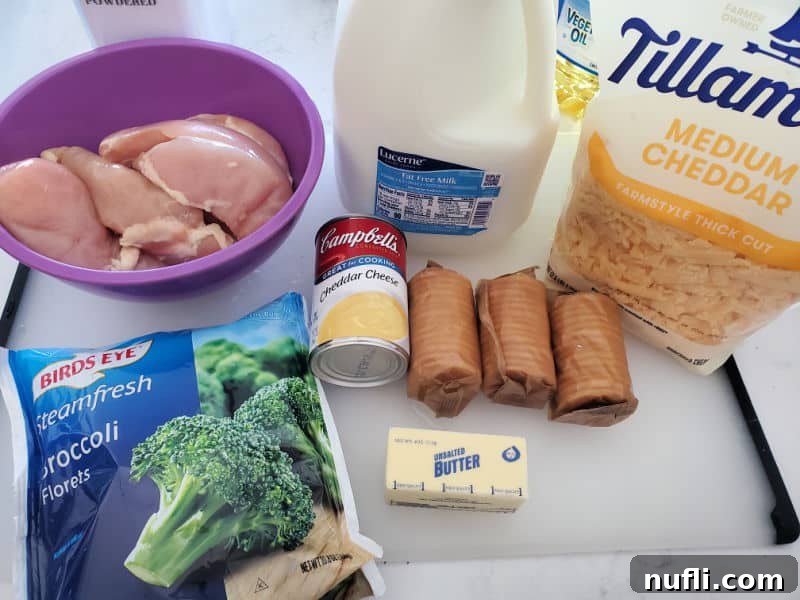 A vibrant flat lay showcasing the raw ingredients for Cracker Barrel Broccoli Cheddar Chicken, including raw chicken breasts in a purple bowl, a glass of milk, a block of cheddar cheese, a bag of frozen broccoli, a can of cheddar cheese soup, a stick of butter, and a stack of Ritz crackers.