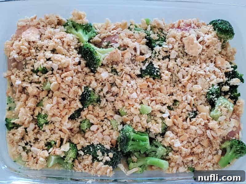 Ritz cracker topping evenly spread over broccoli and chicken in a glass baking dish, ready for the final layer of sauce.