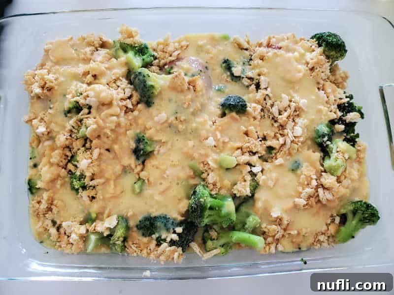 The final layer of cheddar soup mixture covering the Ritz crackers and broccoli in a glass baking dish, ready to be baked to perfection.