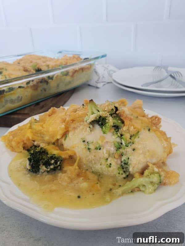 A plated serving of Cracker Barrel Broccoli Cheddar Chicken, showing a perfectly cooked chicken breast topped with broccoli, Ritz crackers, and a rich cheese sauce, with the baking dish visible in the background.