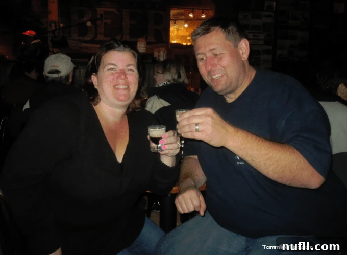 Crafting the Perfect Duck Fart Shot 3 Tammilee and John smiling, holding up their Duck Fart shots in a lively bar setting.